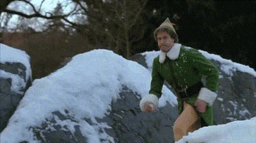 Buddy the Elf in a green costume running through snow and throwing a snowball at the camera.