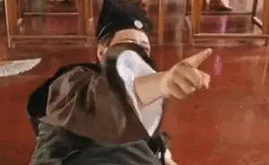 A man in a black traditional Chinese robe points his finger forward with a squinting, playful face, then suddenly throws his head back and falls backward.